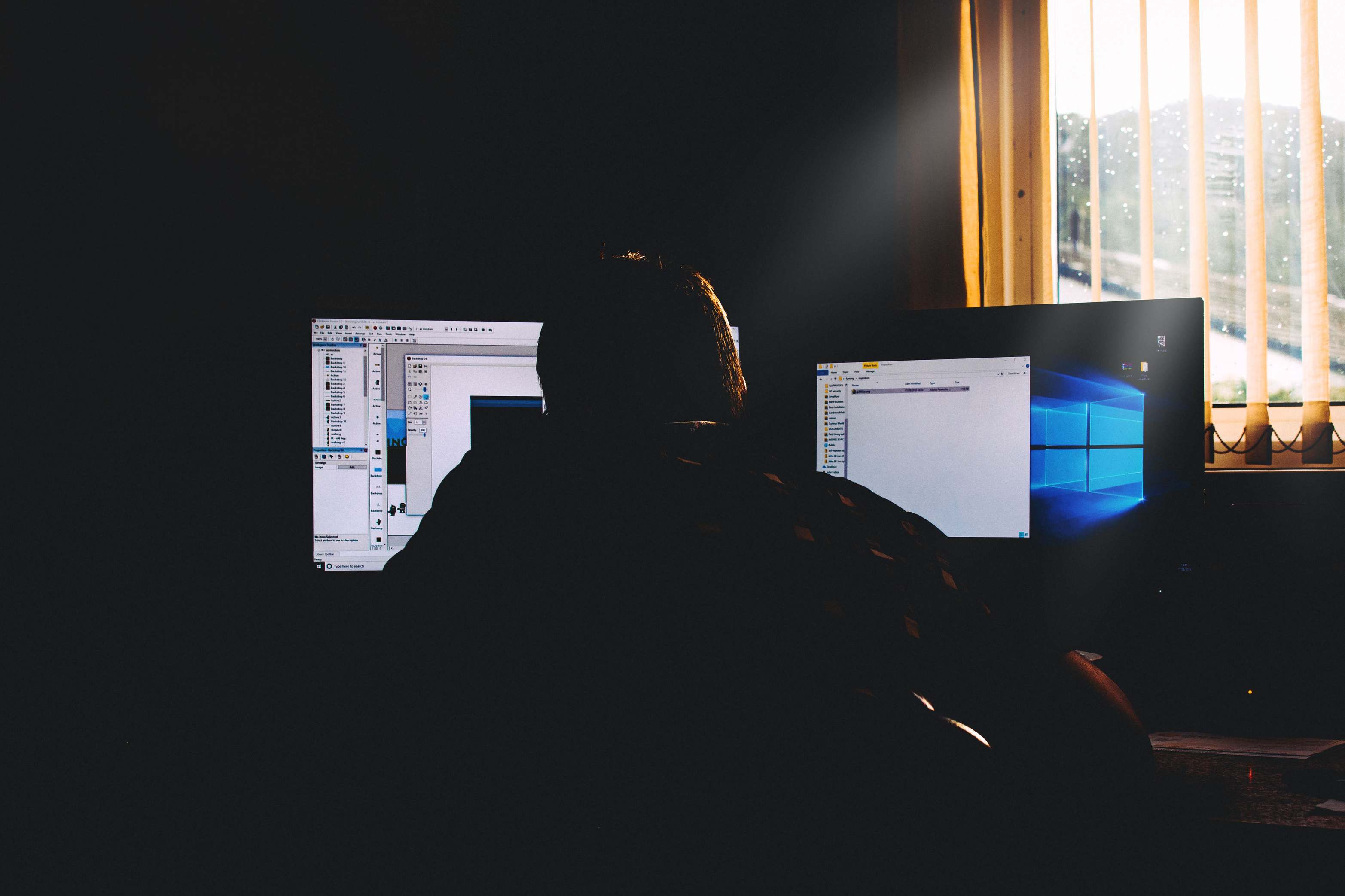 Wide view of a modern office workspace with computers, silhouette of a person working on computers in a dimly lit office environment